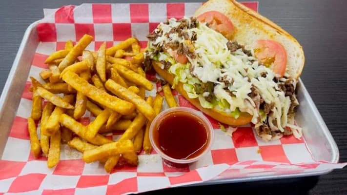 Philly steak sandwich with melted cheese, lettuce and tomato, with fries
